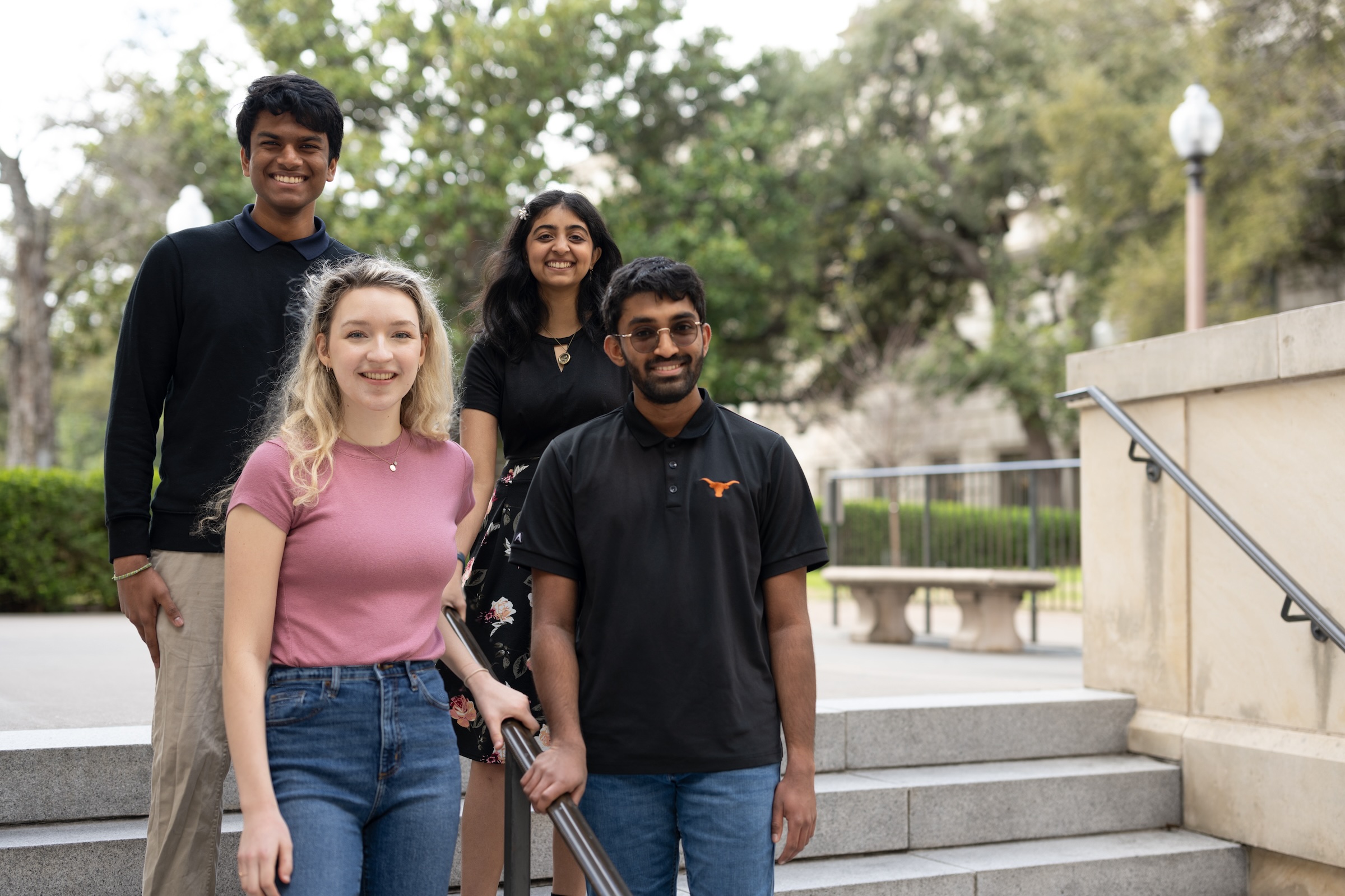 Four students post on a staircase near a limestone building at UT.