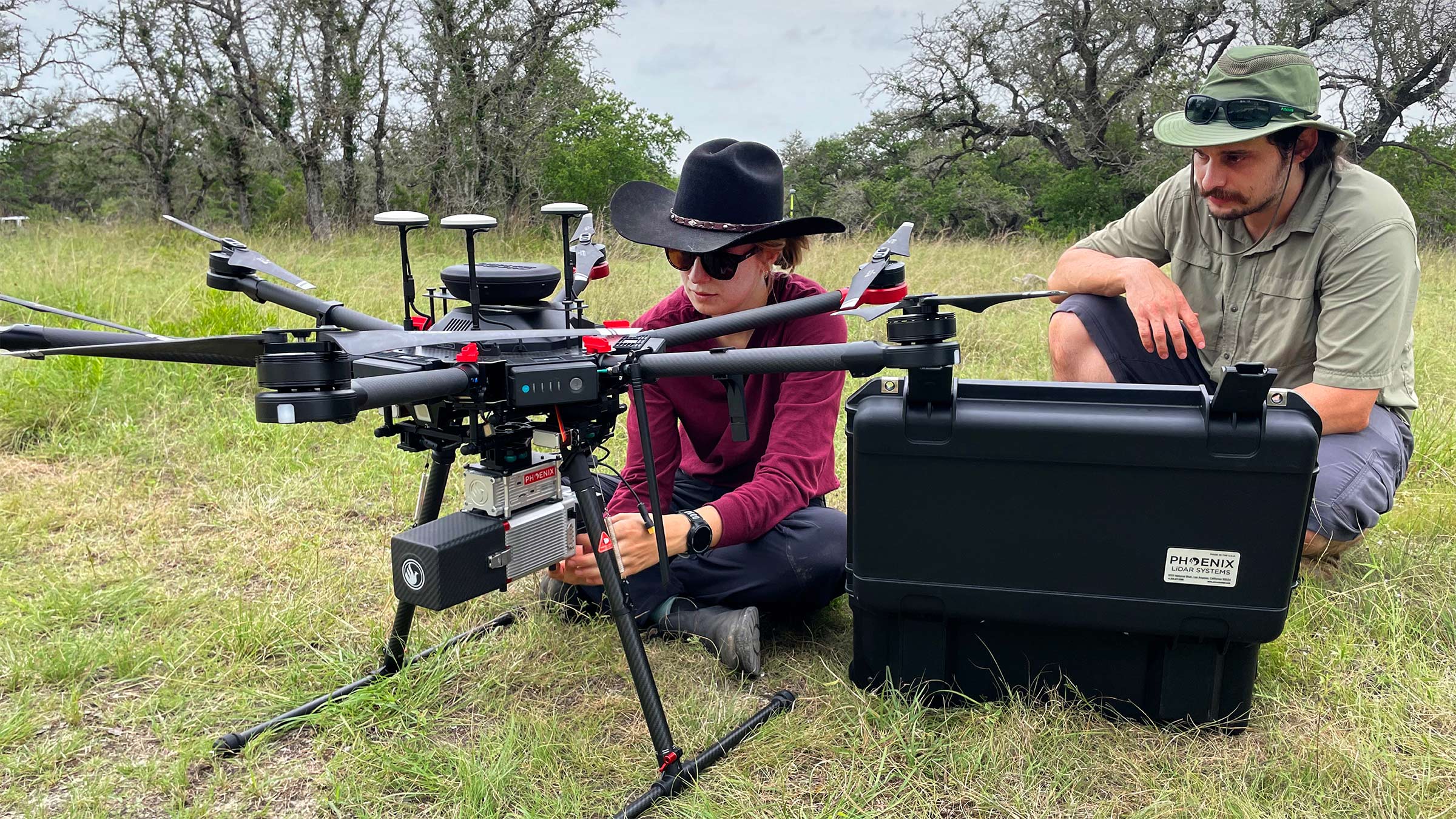 Scientists work with a drone-like machine outside while squatting next to equipment outdoors in the Texas Hill Country