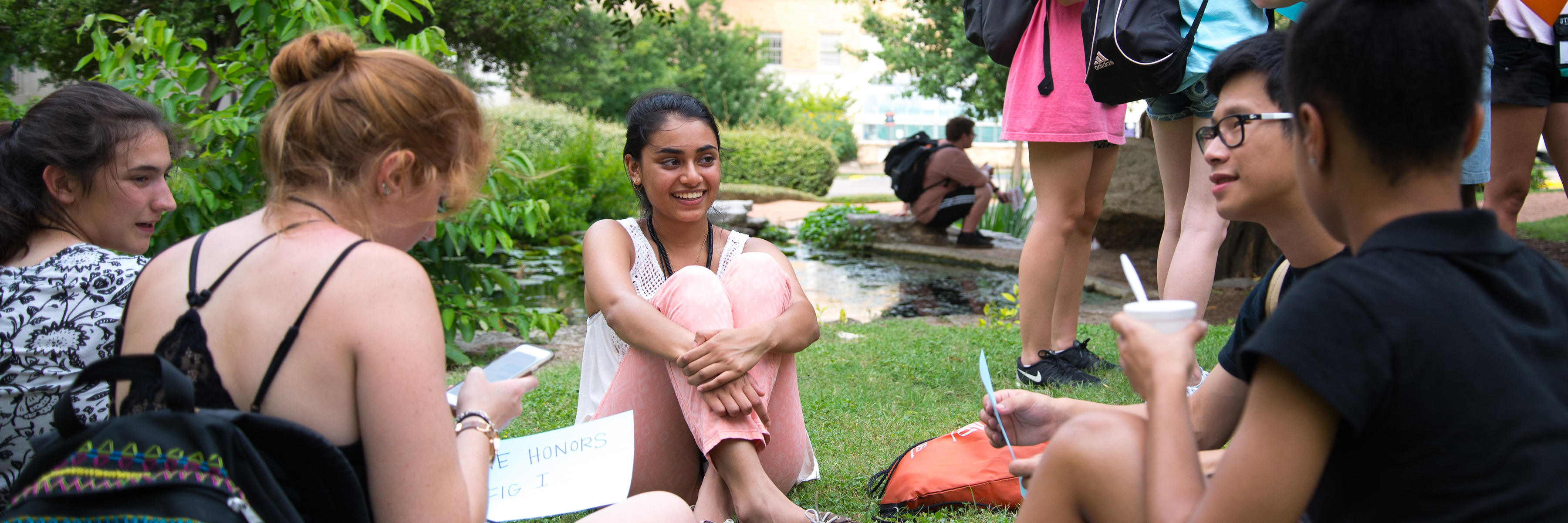 Students sit on grass next to the UT turtle pond.