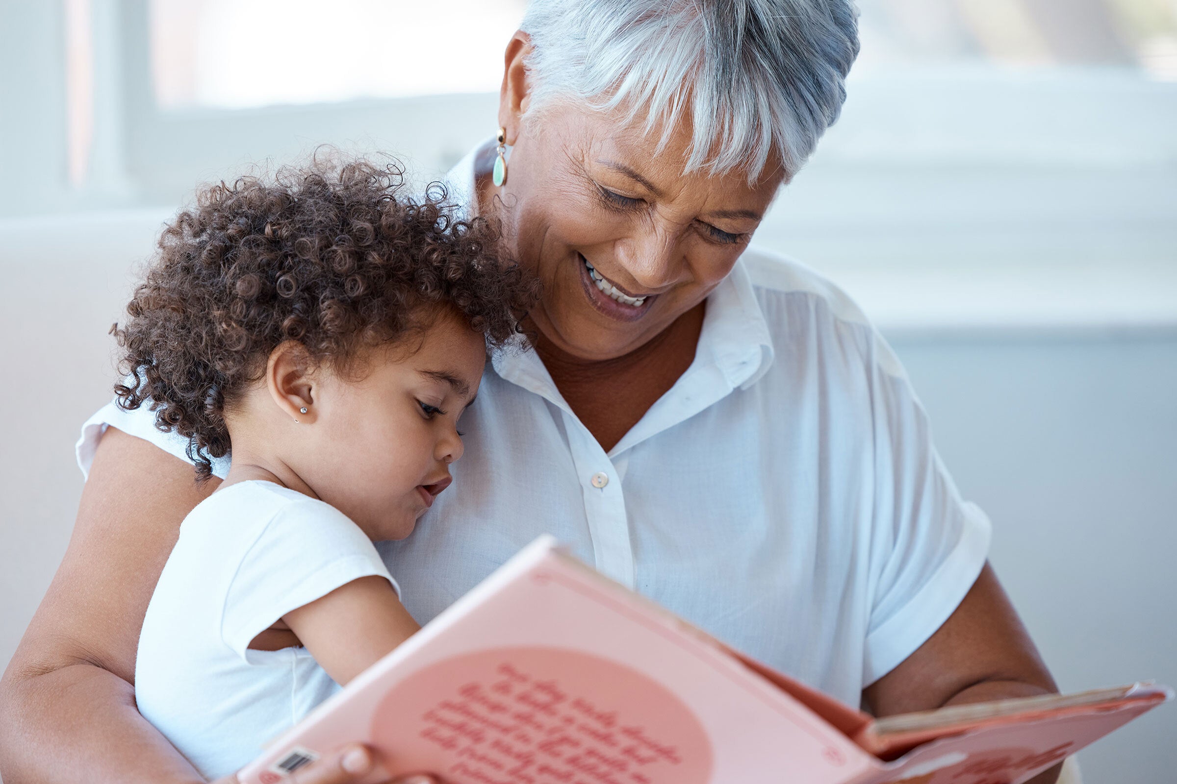 A woman with white hair reads to a child on her lap