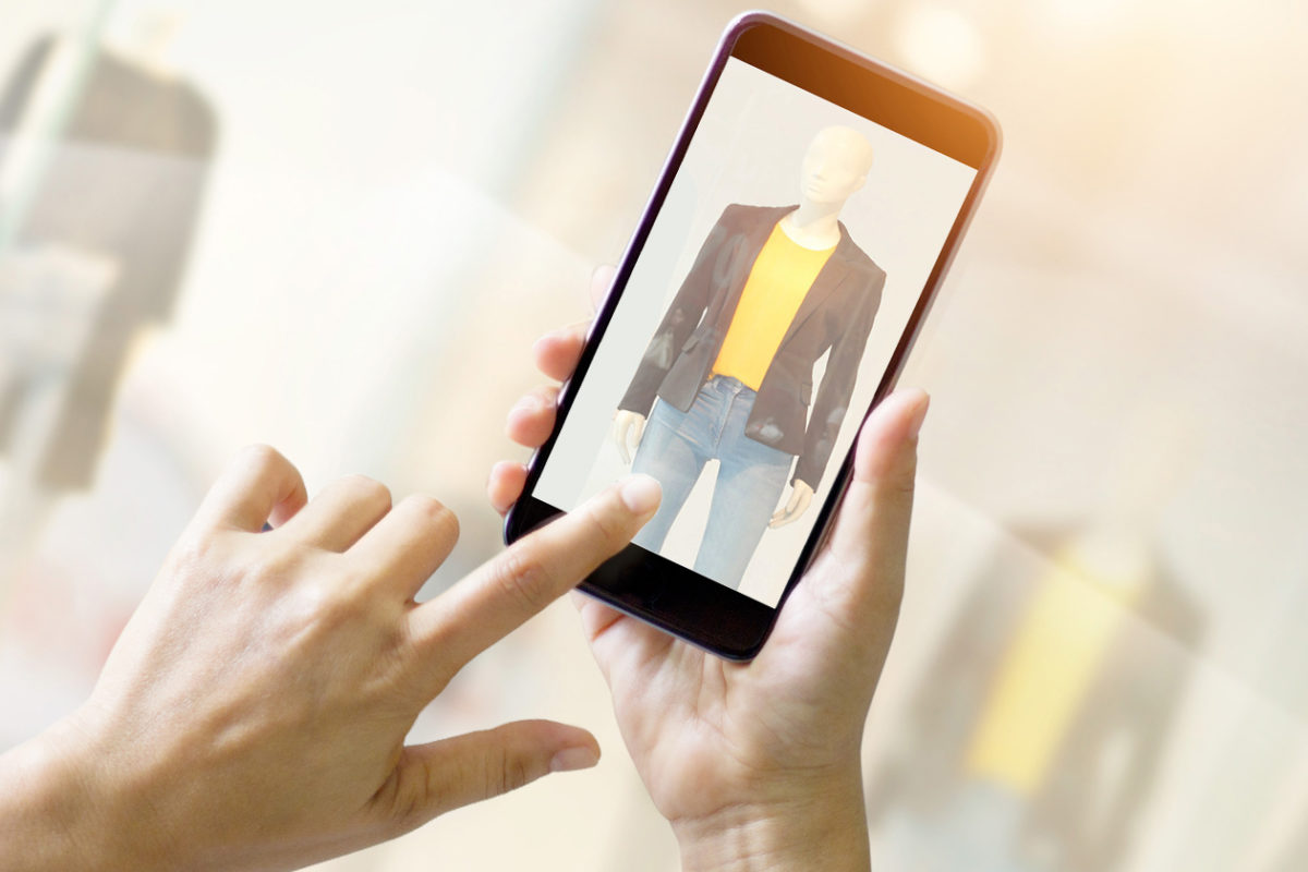 Two hands hold a smart phone which displays a manakin wearing fashionable clothes