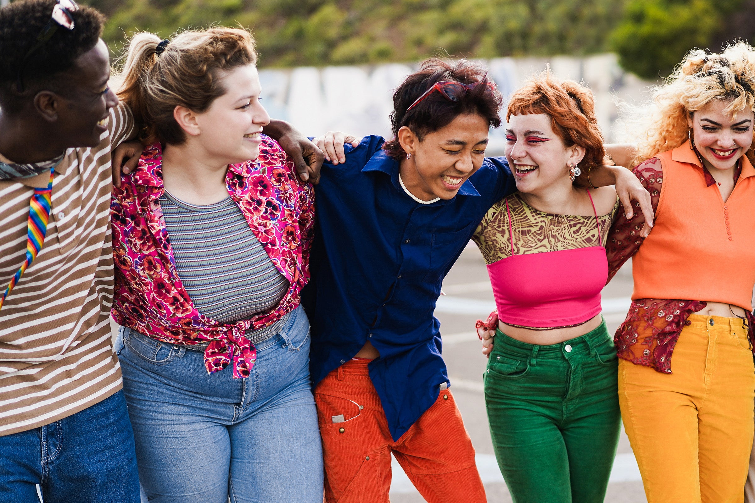 Five teenaged boys and girls stand in a row with their arms around each others' shoulders laughing and smiling.