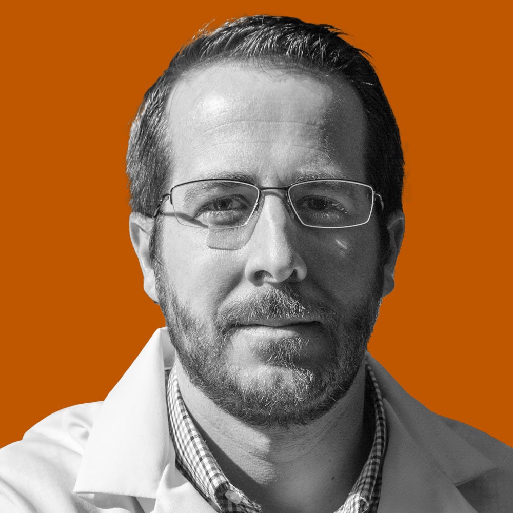 A man in glasses and a lab coat looks at the camera.