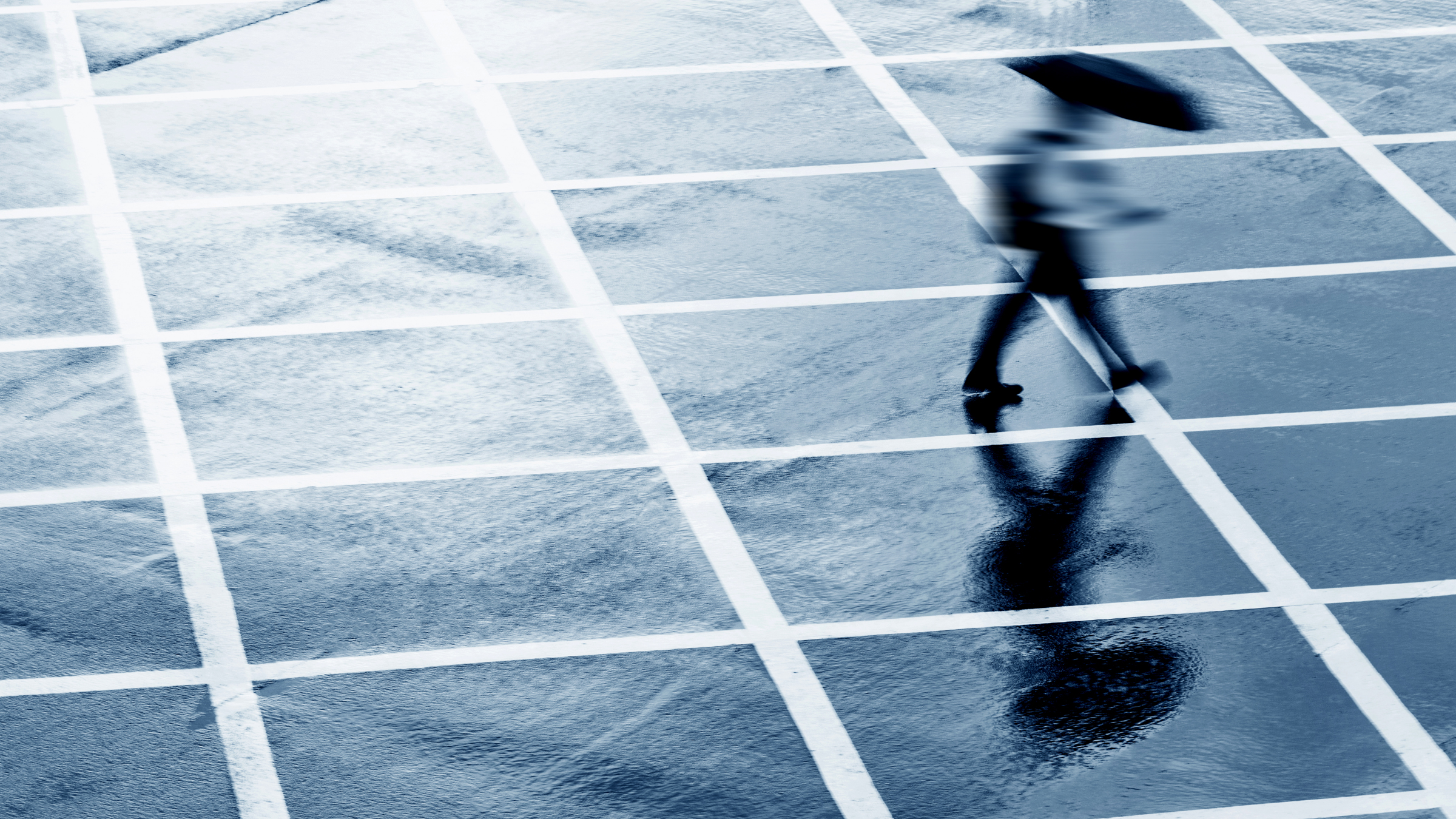 A person with an umbrella walks across a grid of intersecting white lines