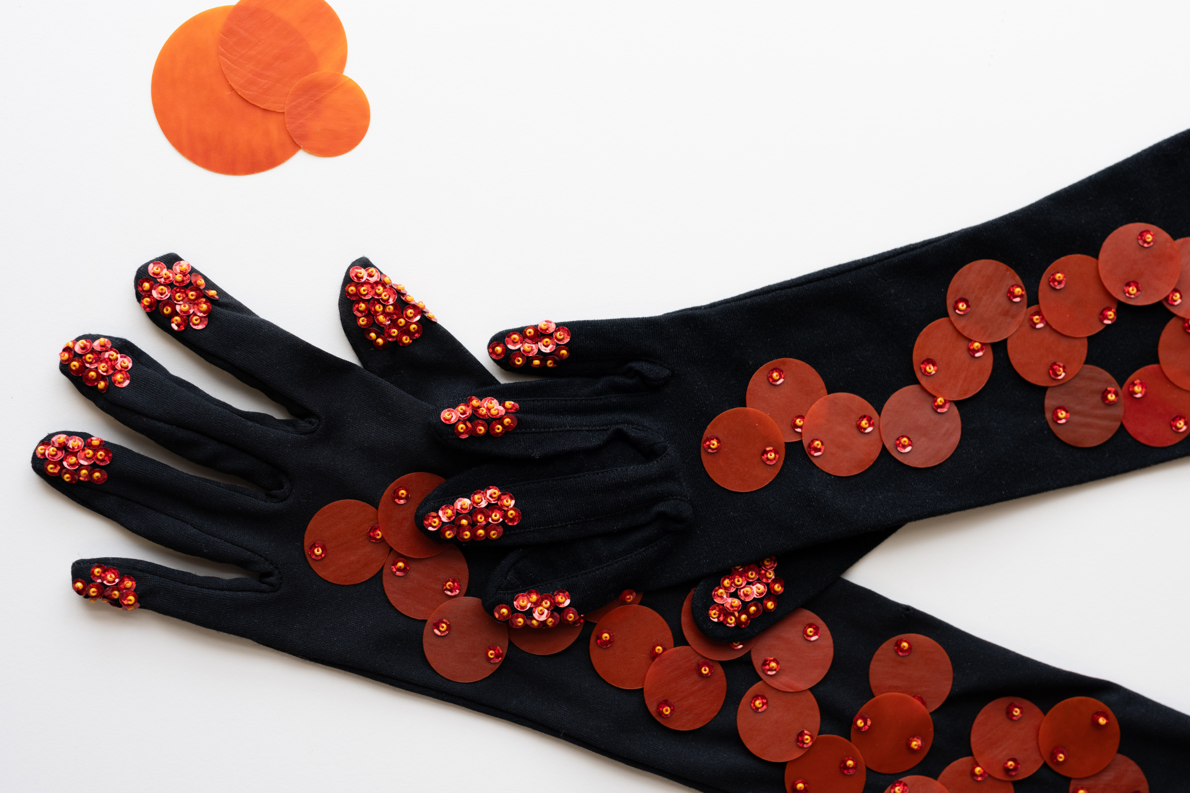 White background with black gloves covered in orange sustainable sequins