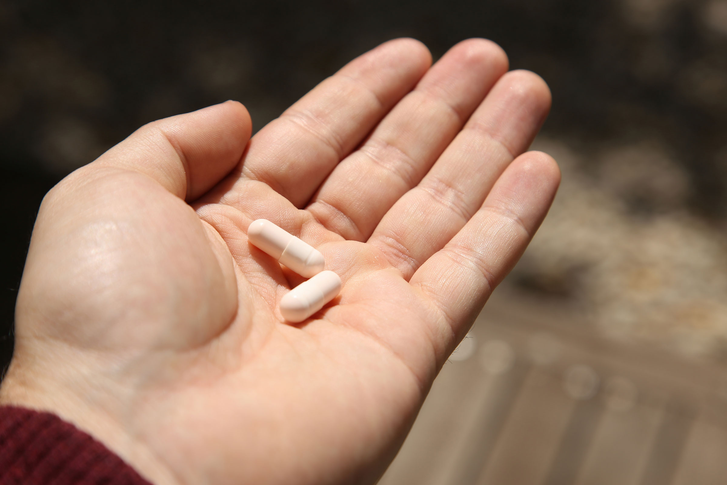 A hand holding two white pills in the palm