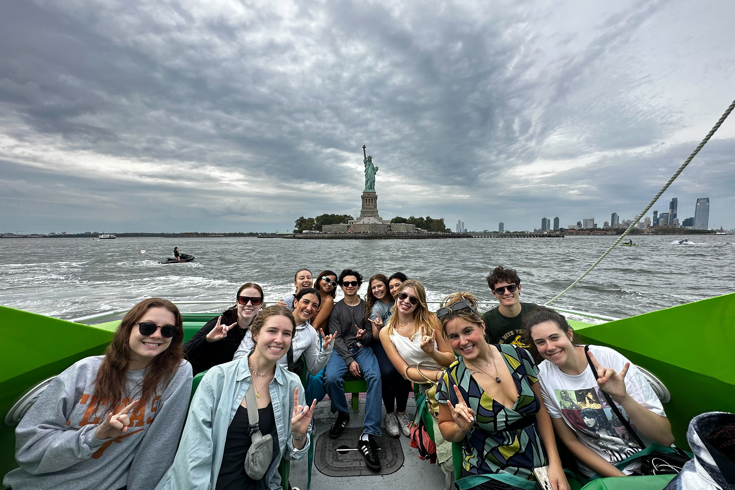 Students holding up hook’em horns signs on a boat in New York City with the Statue of Liberty in the background