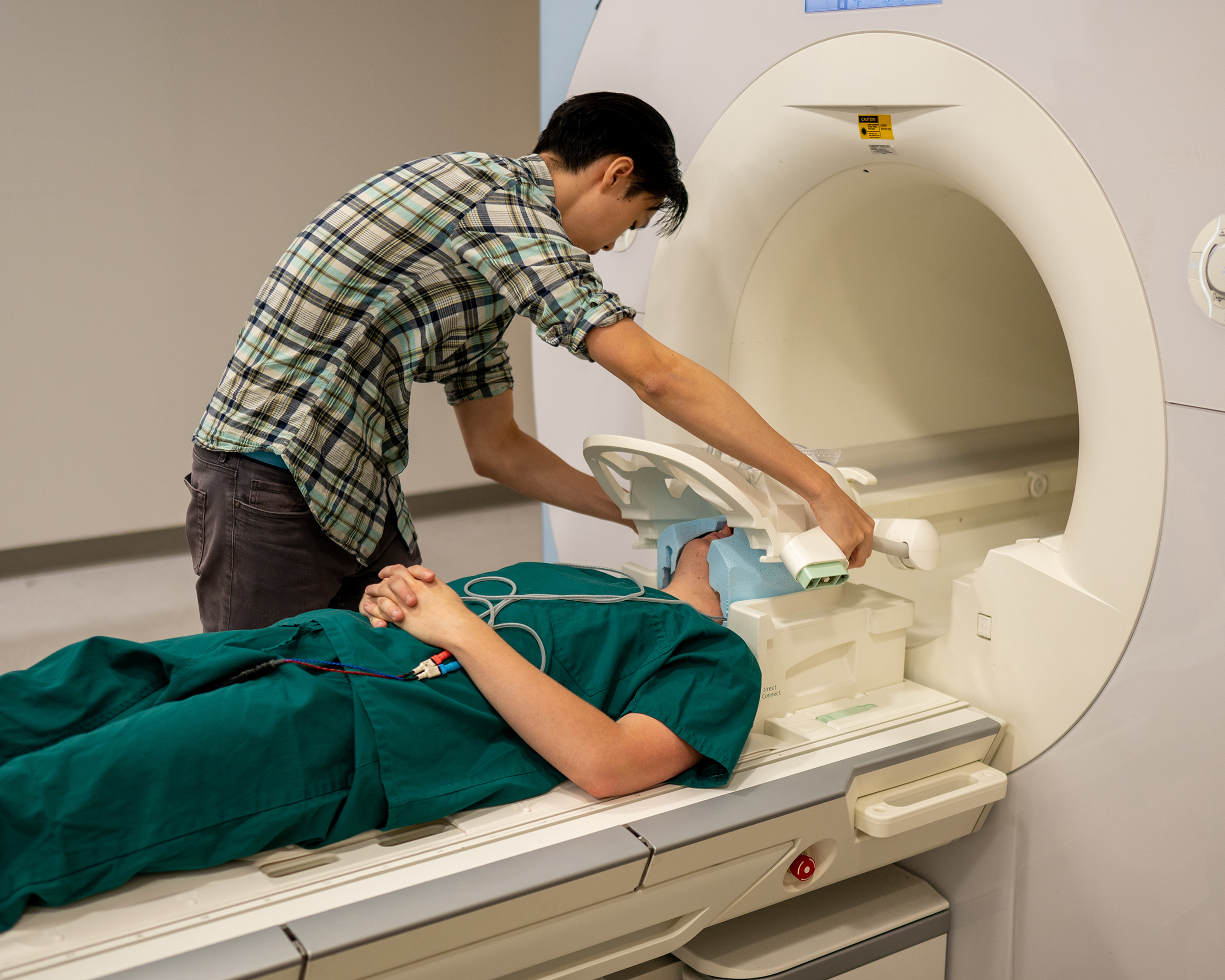 A man places head gear on a participant preparing to go into an MRI scanner