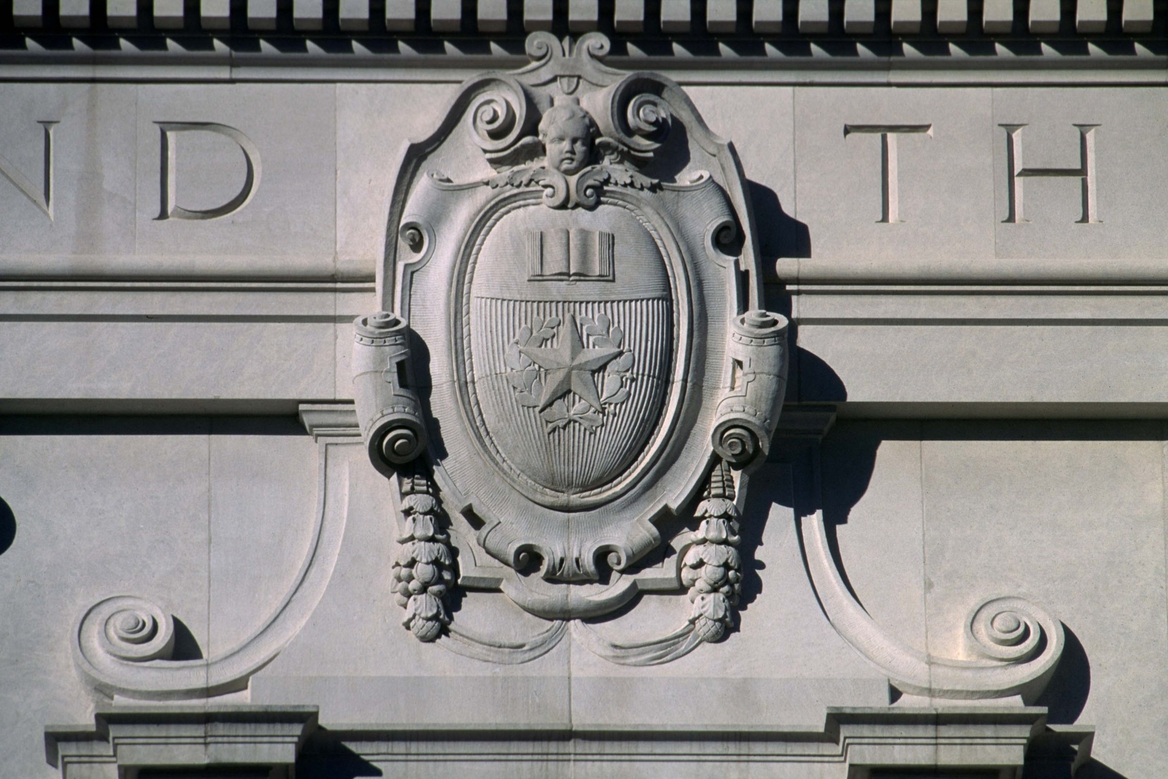 An architectural detail of the University of Texas seal showing a star, book and face cut in limestone on a building
