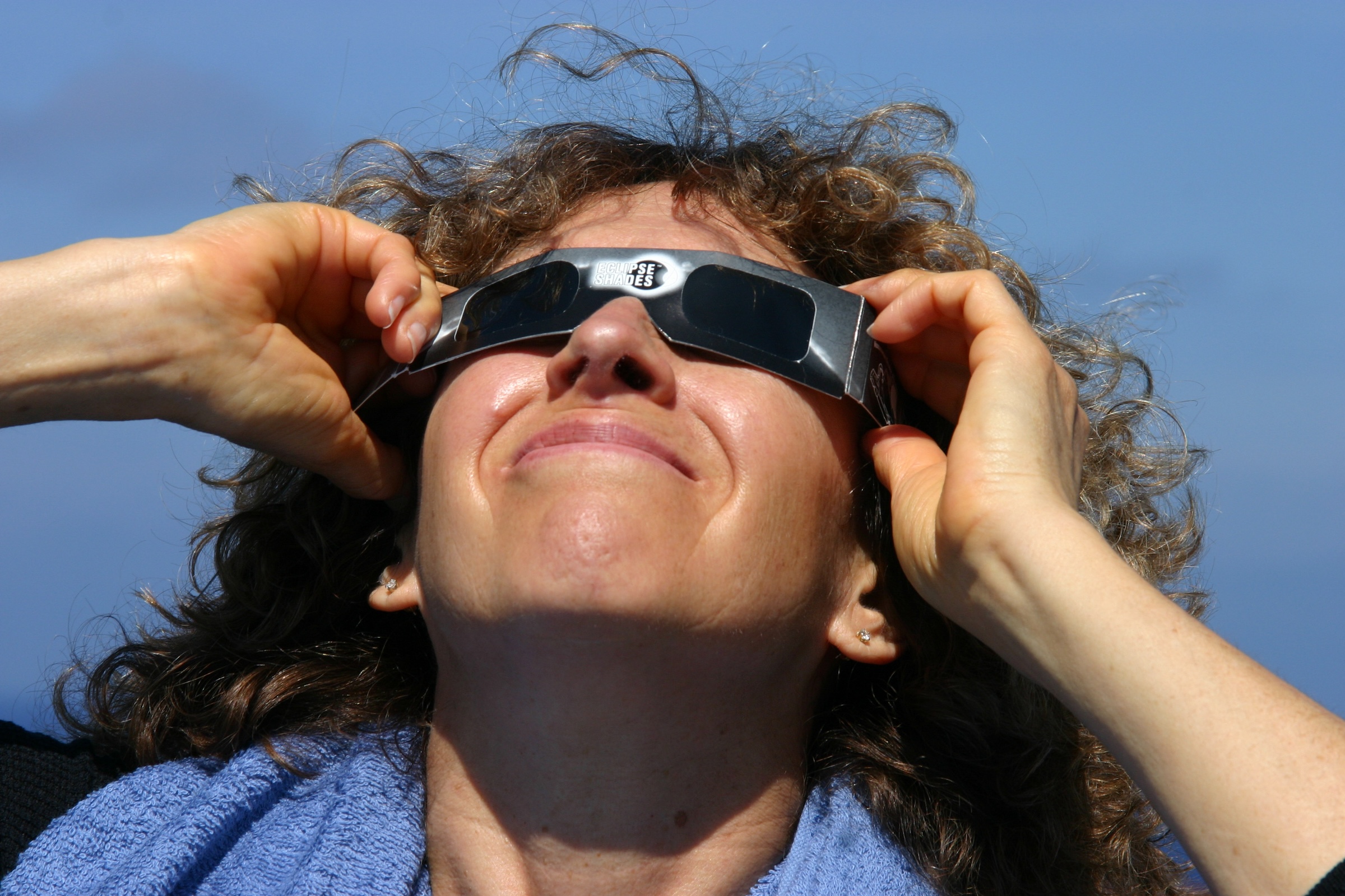 A woman dawns protective eclipse glasses and looks at the sun on a cloudless day